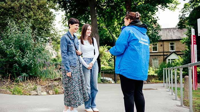 A student ambassador talking to 2 visitors at an open day.