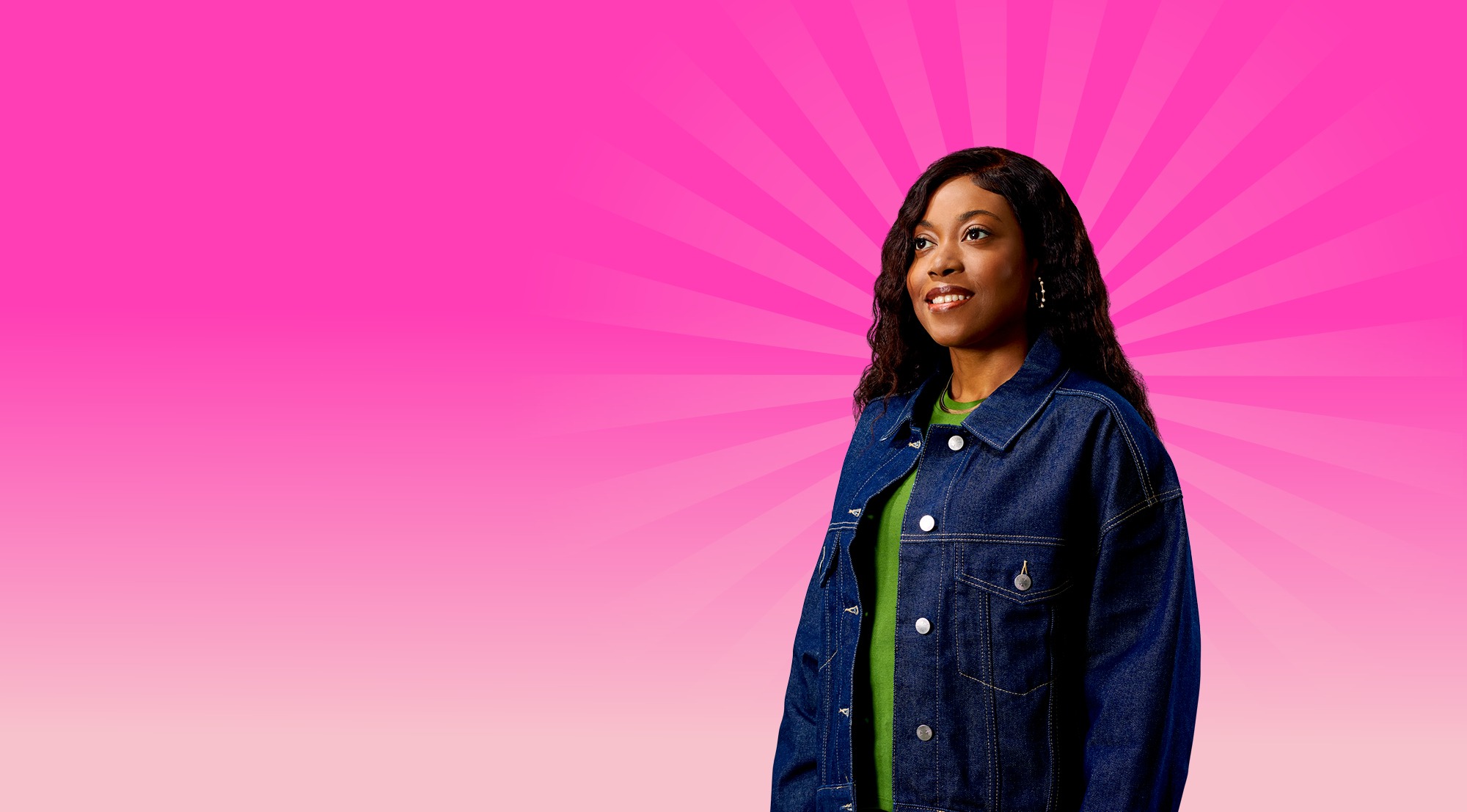 A female student standing against a bright pink starburst background, wearing a denim jacket and green top.