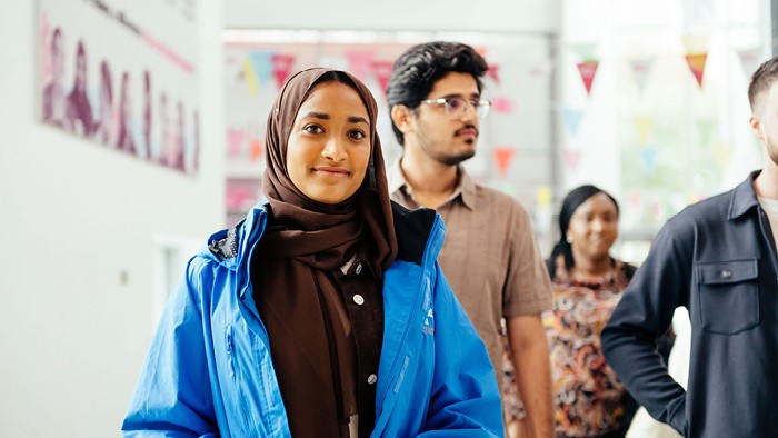 An open day student ambassador in a brown hijab and blue jacket leading an open day tour with a group of attendees.