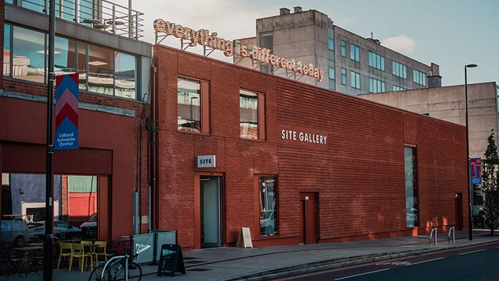 Exterior of Site Gallery in Sheffield. A flat brick facade with an illuminated sign on the roof that reads "Everything is different today"