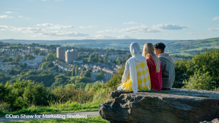 Students sitting in a park outdoors overlooking peak district scenery