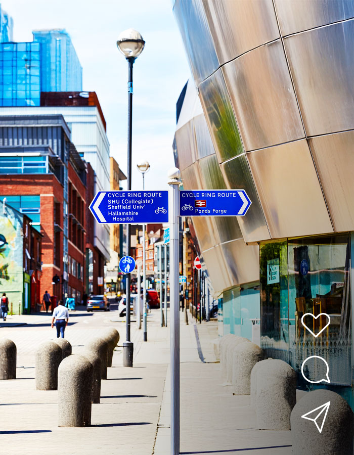 Blue cycle route signs on a city street pointing towards Sheffield Hallam University, Sheffield University, Hallamshire Hospital and Ponds Forge.