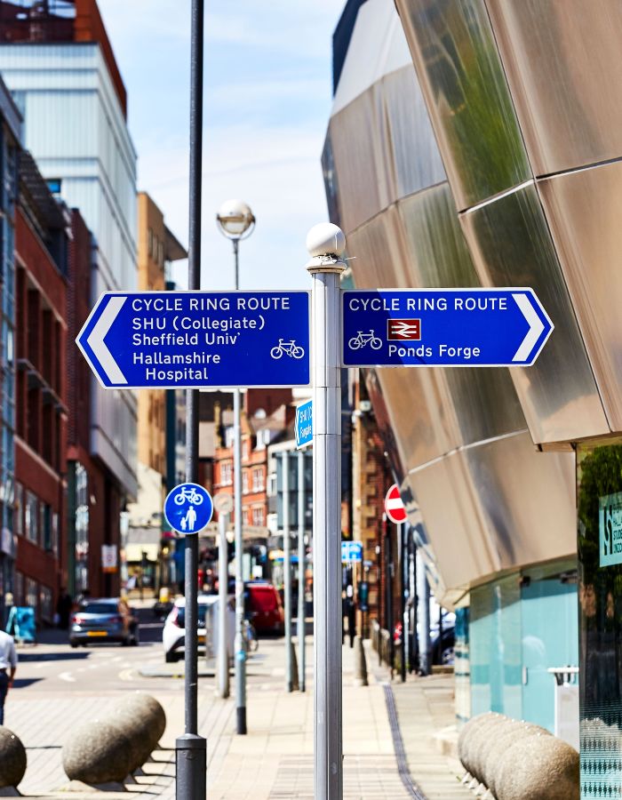 Two blue cycle route signs on a street, pointing to local destinations in Sheffield city centre.