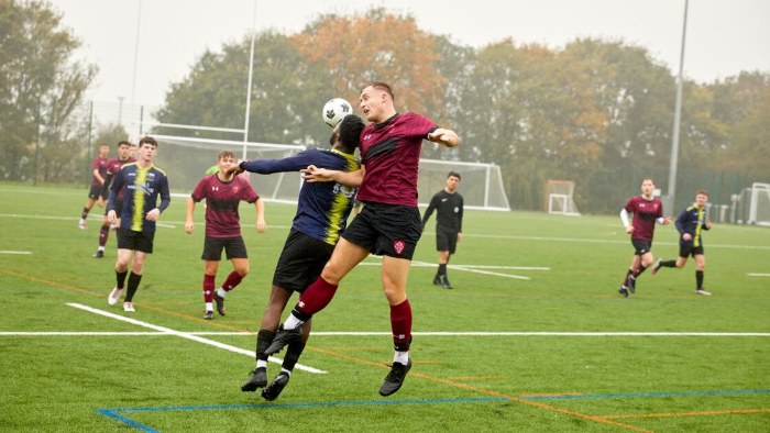 Two football players jumping to head the ball during a match on a Sheffield Hallam sports pitch.