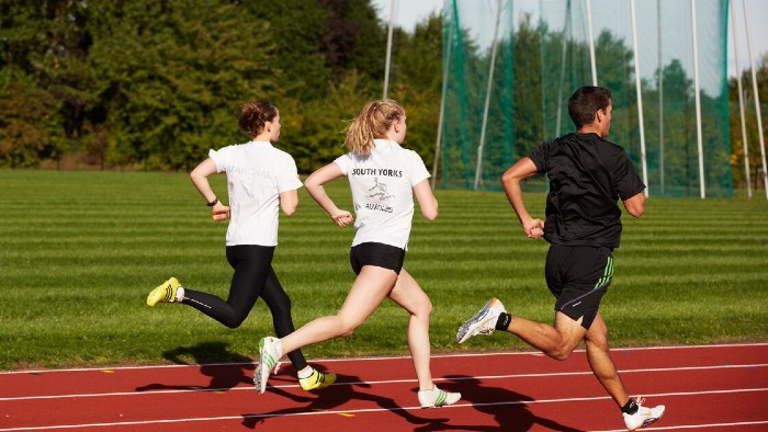 Three students running on an athletics track.