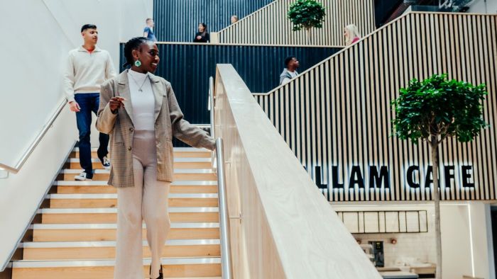Students walking up and down a wide wooden staircase in a modern office space at city campus with Hallam Cafe nearby.