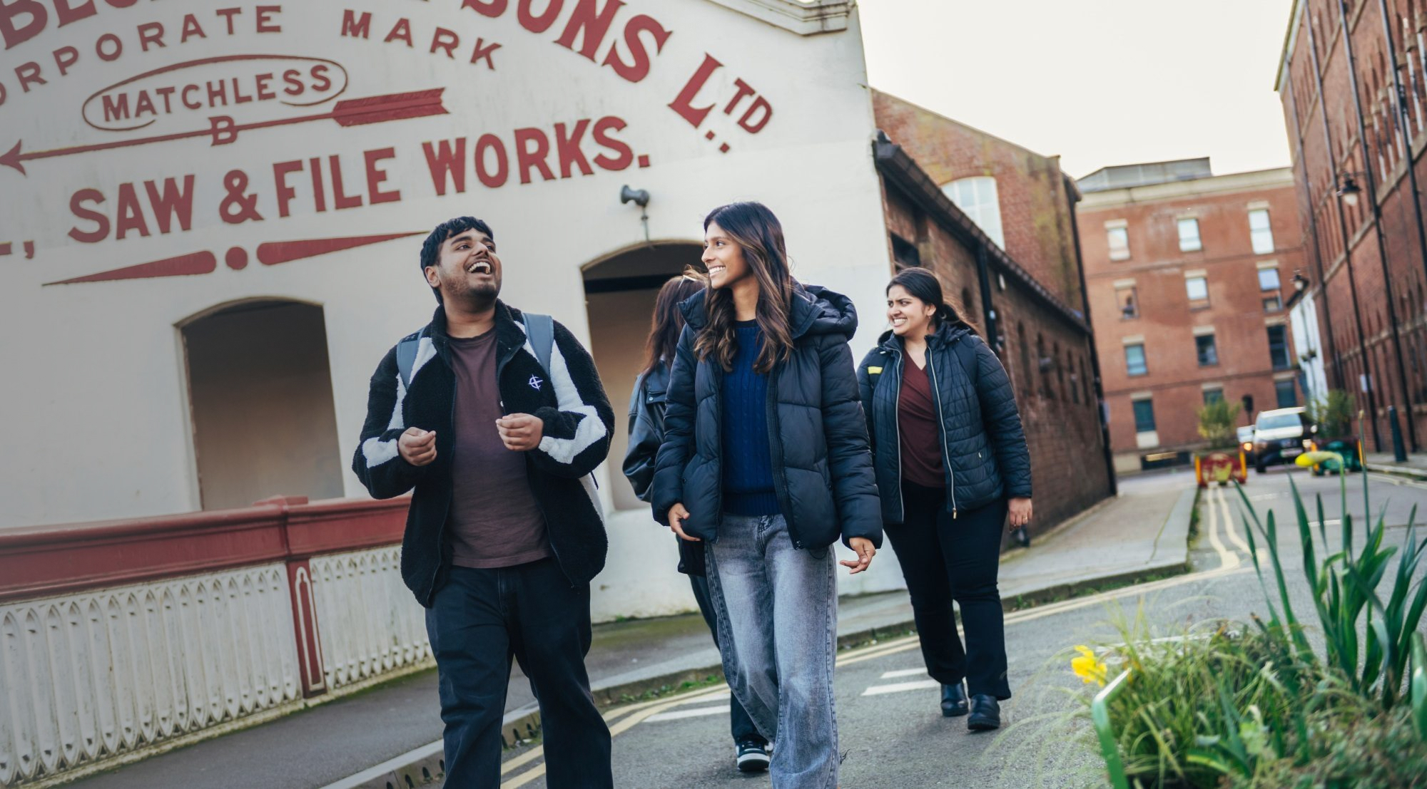 A group of people walking and smiling together down a street lined with brick buildings.