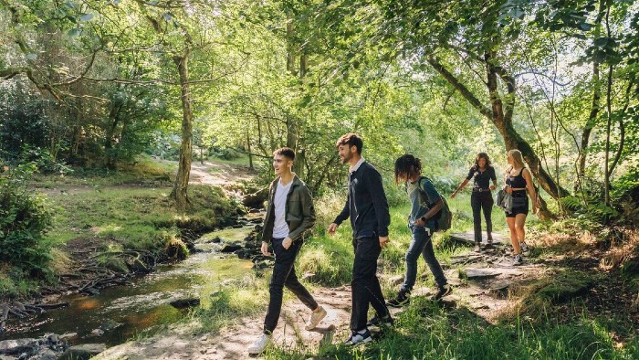 A group of students walking through woodland towards a river