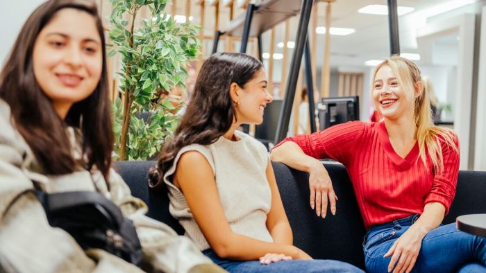 Three people sitting on a sofa in a modern indoor space, engaged in conversation.