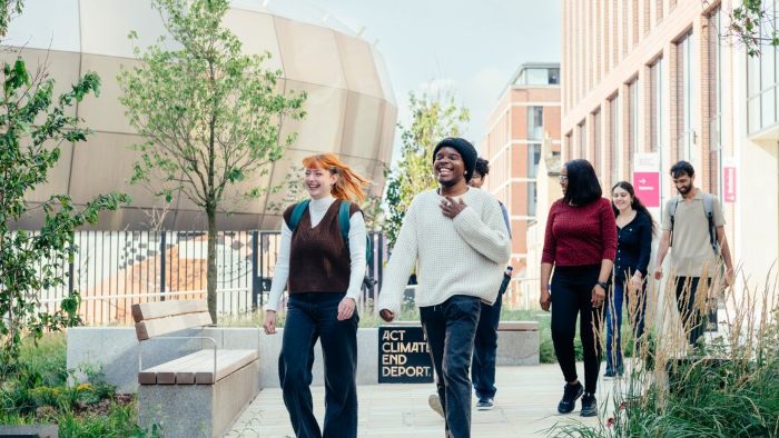 A group of students walking through Hallam Green with benches, plants, and the City Campus buildings in the background.