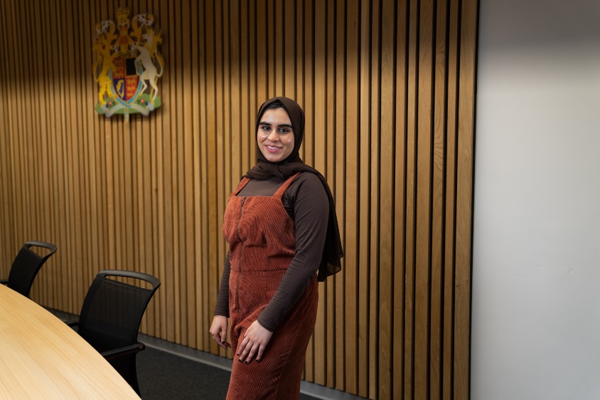 Fozia Sultana standing in front of the University crest in the Moot Court
