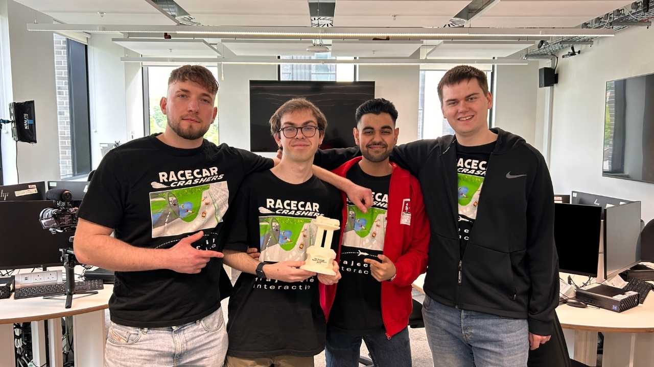 Four male students are stood together and wearing black t-shirts with the words 'Racecar Crashers' printed on. The student in the middle is holding a white trophy.