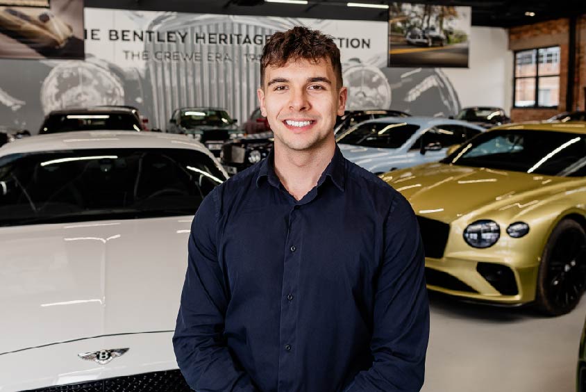 Kasper wearing a shirt, stood in front of Bentley Cars