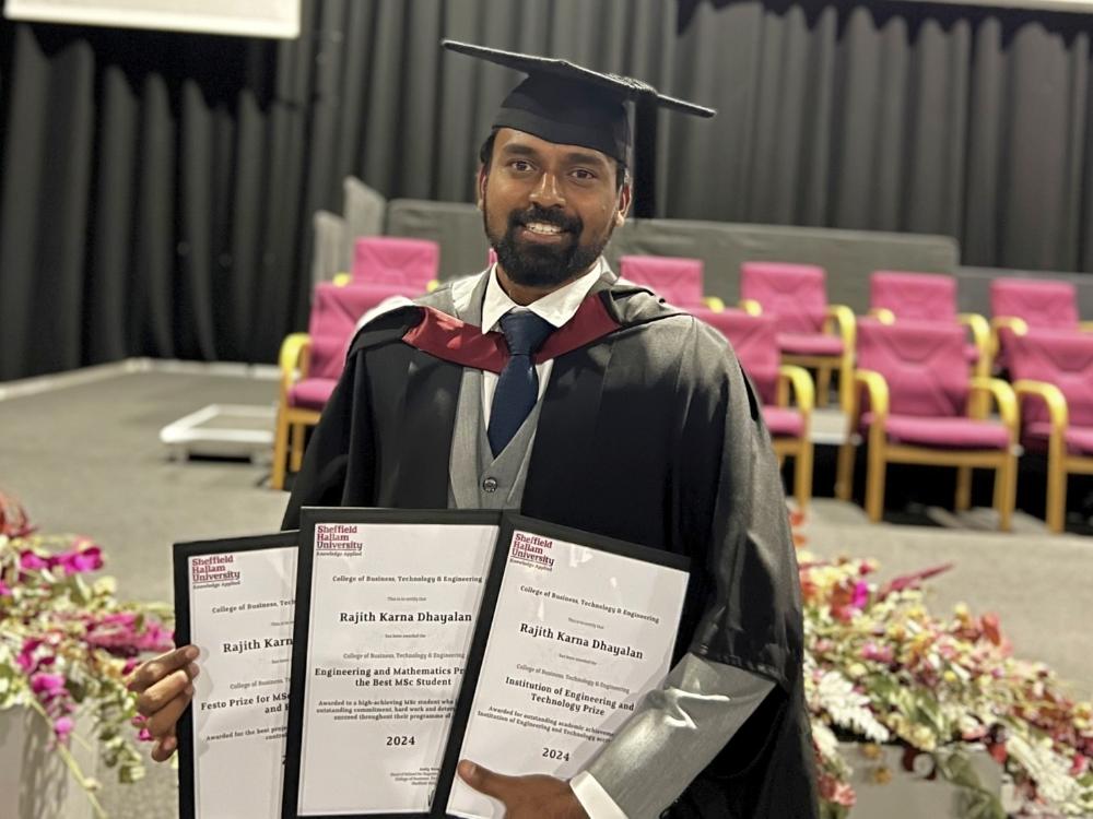 Rajith is smiling and wearing a graduation cap and gown over a grey suit and tie, holding three award certificates.