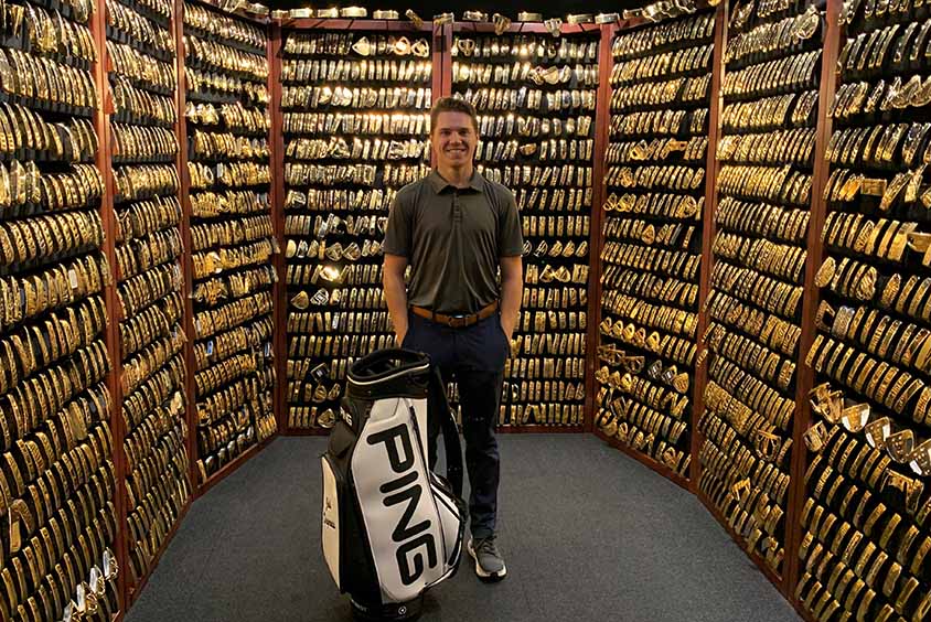 Student Josh stood in a room full of golf clubs on shelves with a golf bag next to him
