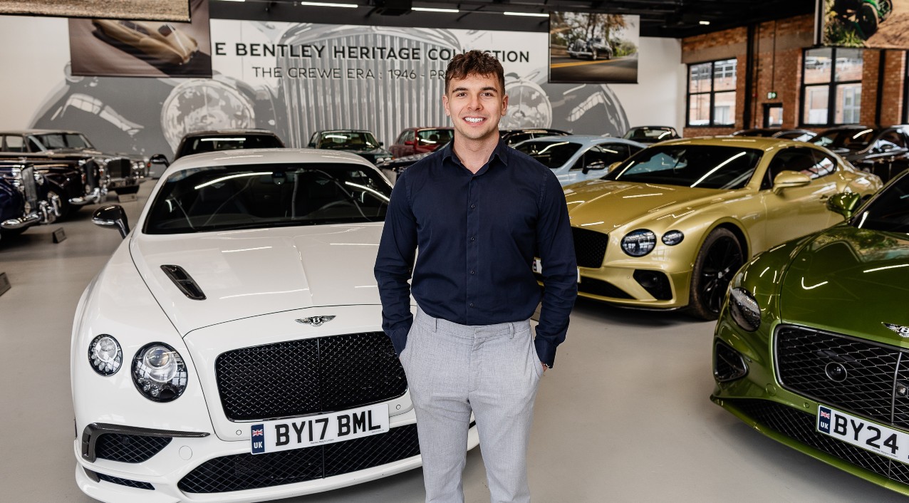 Male with standing in front of Bentley cars smiling at the camera.