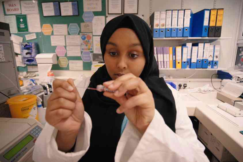 Female student wearing a headscarf and lab coat looking at a blood sample in a lab.