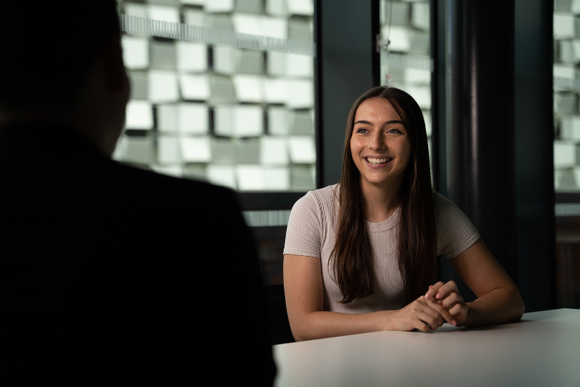 Woman smiling and facing a person across from table.