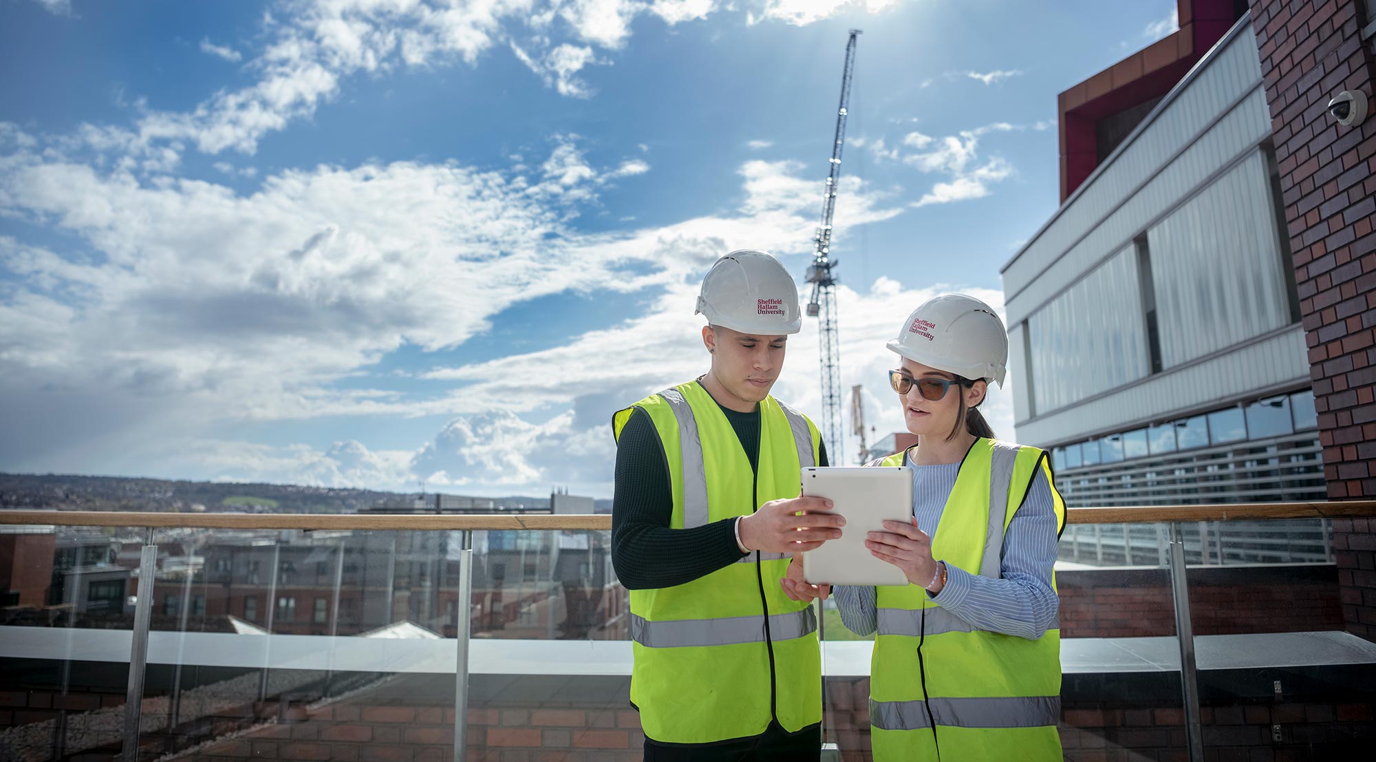 Two Sheffield Hallam placements students stood on site holding and discussing building plans.