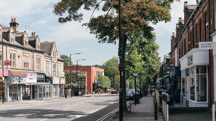 A view down tree lined Ecclesall Road on a sunny day. Several bars, boutique shops and eateries can be seen on either side.