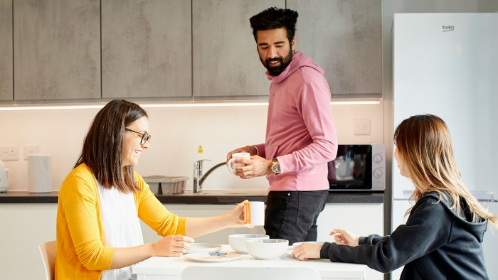Group of students - two seated - chat together in the kitchen of their accommodation.