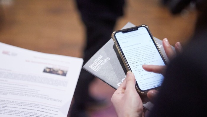 White hands holding a phone above some paper. 