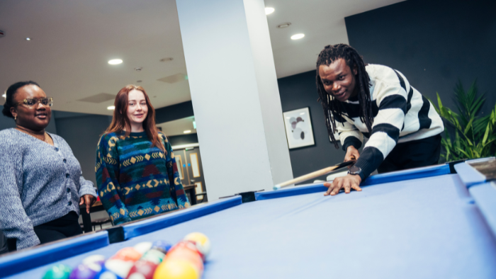 Three students playing pool in a Sheffield Hallam accommodation common room.