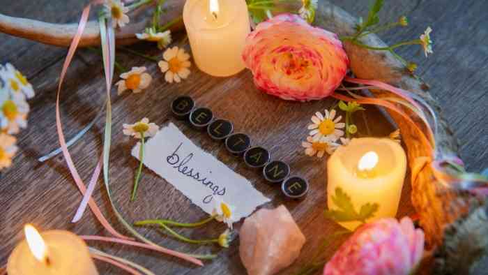 A photo of an arrangement of lit candles, wooden wreaths, natural materials and buttons spelling out Beltane with the word blessings written on a piece of paper below. 