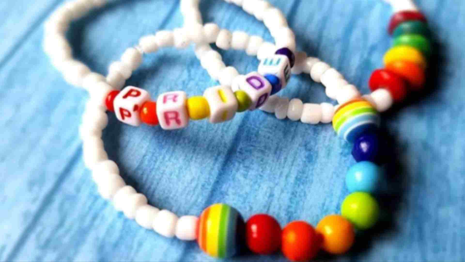 Photo of bracelets made from plastic rainbow beads with one spelling out PRIDE on a wooden surface.